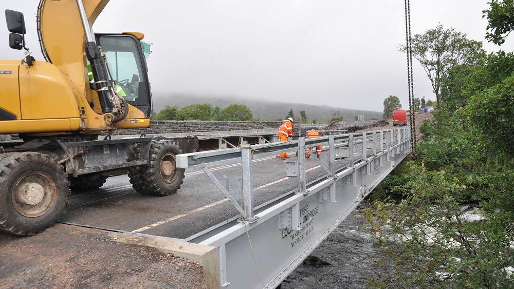 A construction worker is focused on building a bridge, wearing safety gear and using tools amidst a construction site.